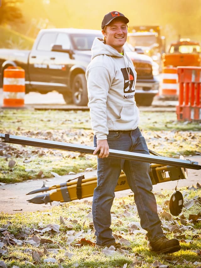 Sommerset employee working outside while smiling and holding construction tools