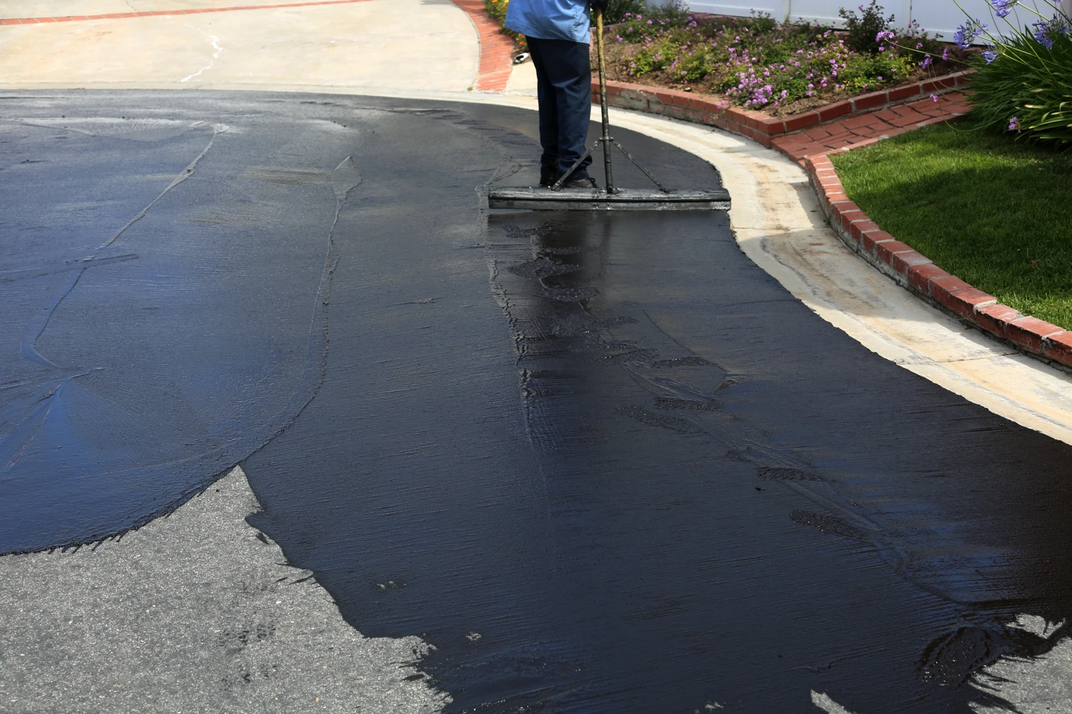 Worker Applying Fresh Asphalt To A Damaged Driveway